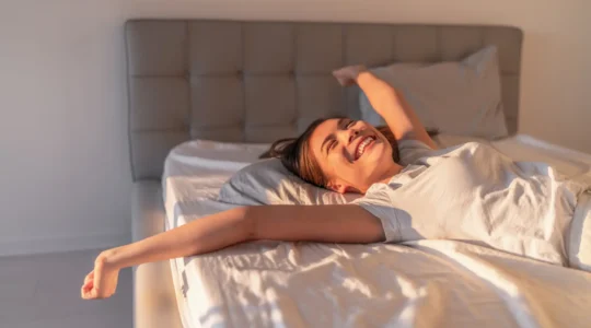 Une conseillère soulève la surface quiltée d'un matelas haut de gamme pour montrer les ressorts ensachés et les couches de matériaux naturels, dans une chambre élégante à la française.
